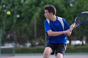 teenage boy swinging a tennis racket at a ball